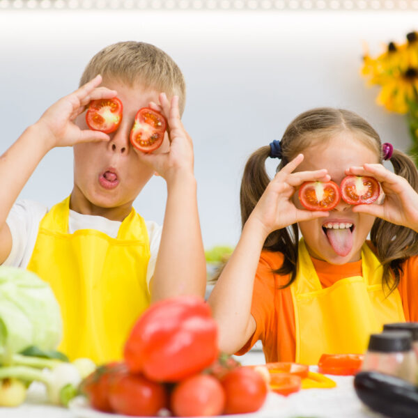 Happy kids having fun with food vegetables at kitchen holds tomatoes before his eyes like in glasses.