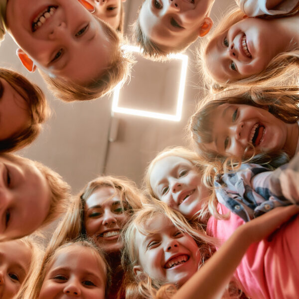 Group of positive boys and girls with their female dance teacher. Bottom view of happy children smiling at camera while standing in the dance studio. Friendship