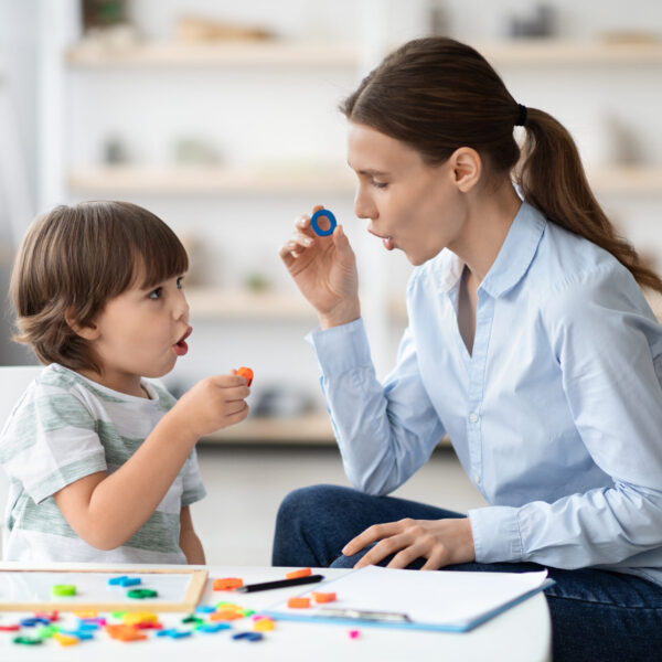 Female speech therapist curing child's problems and impediments. Little boy learning letter O with private English language tutor during lesson at office